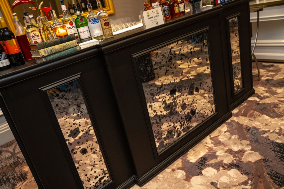 Bar with dark wood paneling and cowhide pattern inserts, bottles on shelves above, patterned carpet below