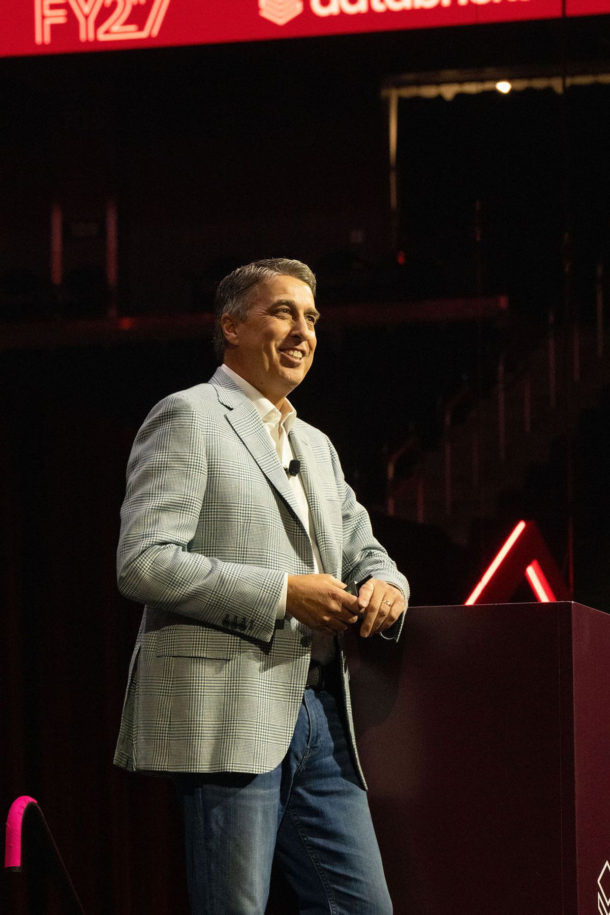 Speaker in gray blazer presenting at podium with Databricks branding and neon lighting at conference