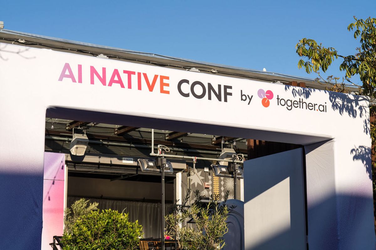 White conference tent with "AI NATIVE CONF by together.ai" signage under blue sky with trees visible