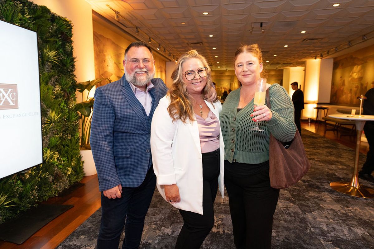 Three people pose together smiling at a networking reception in an upscale venue with decorative lighting.
