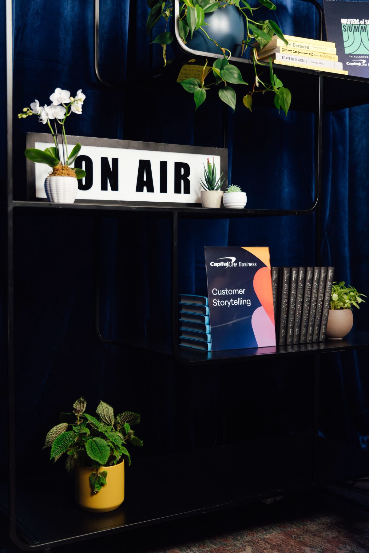 Dark blue shelving unit with books, plants, and "ON AIR" lightbox sign displayed on multiple shelves