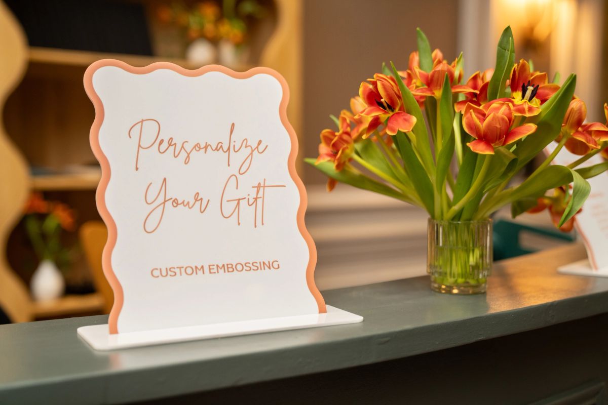 White decorative sign reading "Personalize Your Gift Custom Embossing" displayed on counter next to orange.