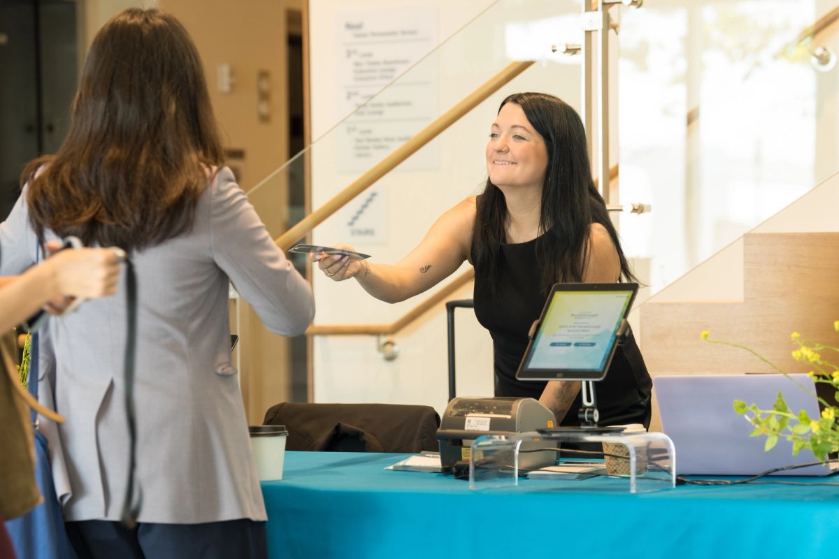 Conference attendee receives materials from smiling staff member at blue registration table in lobby