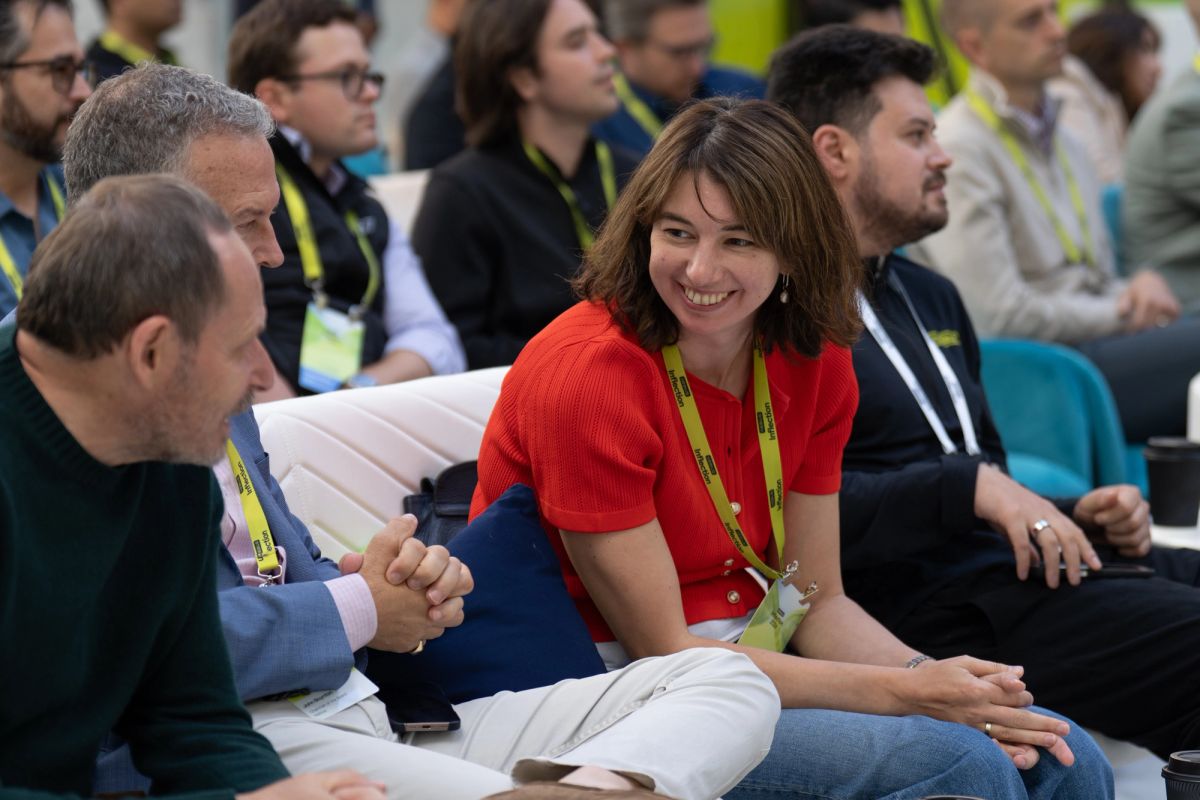 Attendees networking at a conference, woman in red top smiling during conversation.