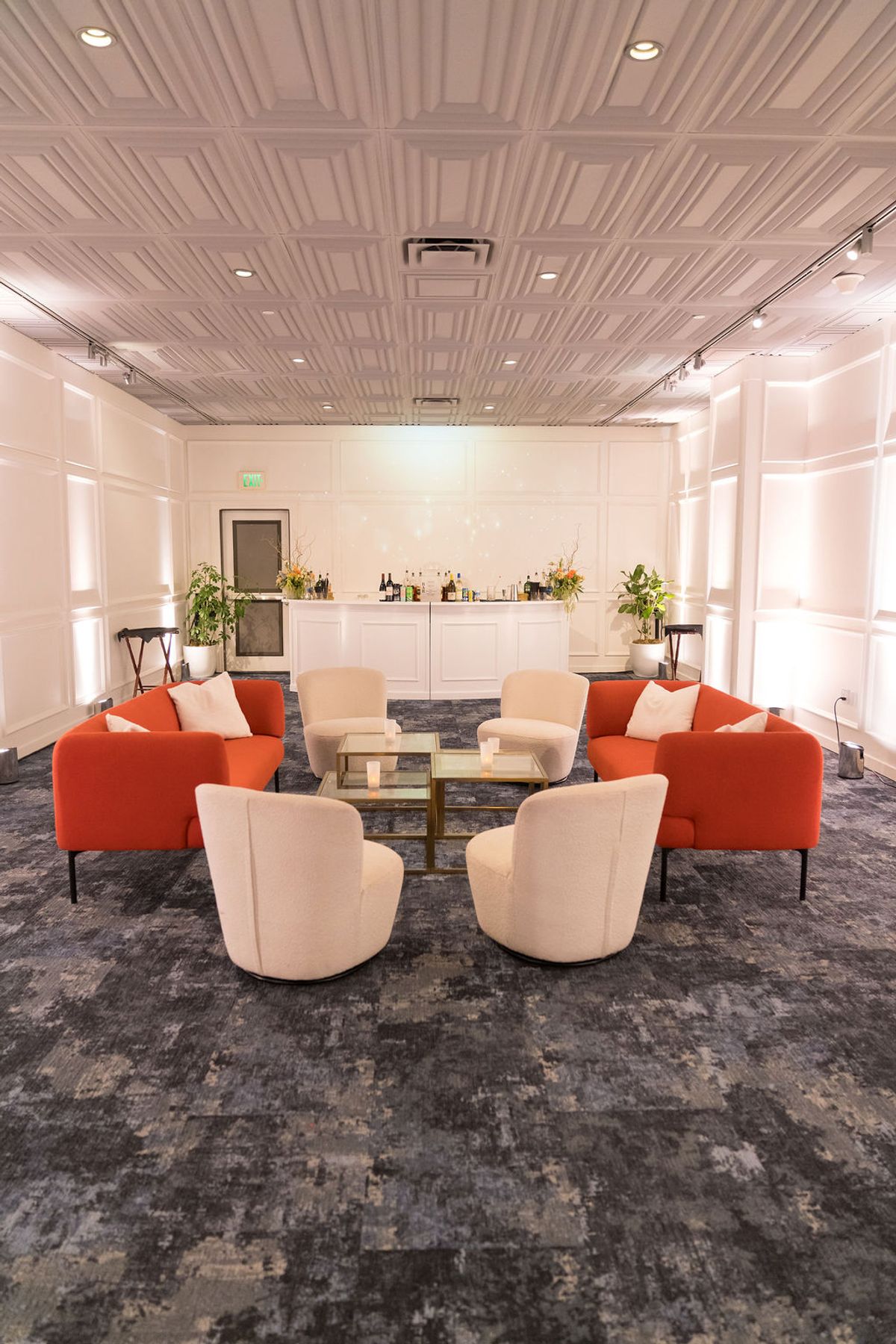 Elegant lounge area with orange and beige seating arrangement around glass coffee table, white bar in.