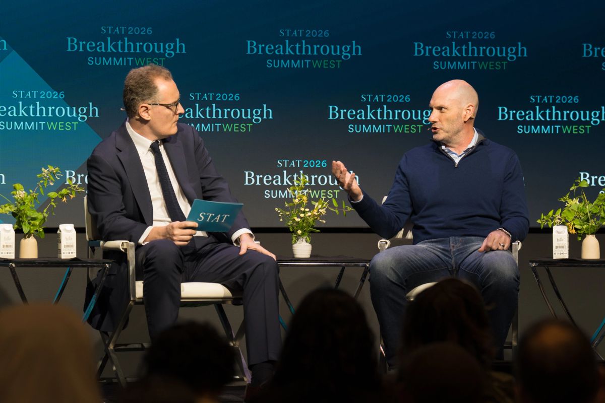 Two men in conversation on stage at Breakthrough Summit West event, one in suit, one in casual wear