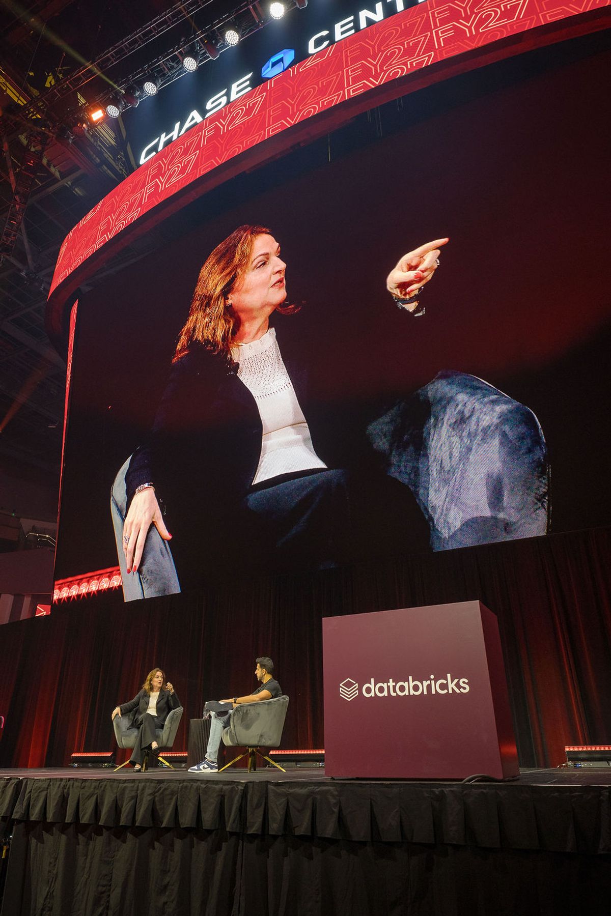 Speaker gesturing on stage at Chase Center conference with Databricks branding, audience member visible below