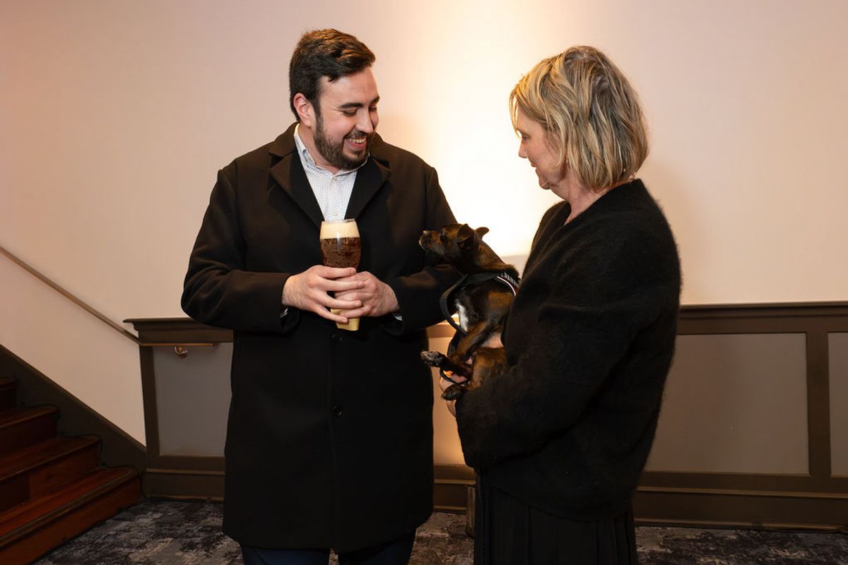Two people networking at a reception, one holding a drink, the other holding a small dog