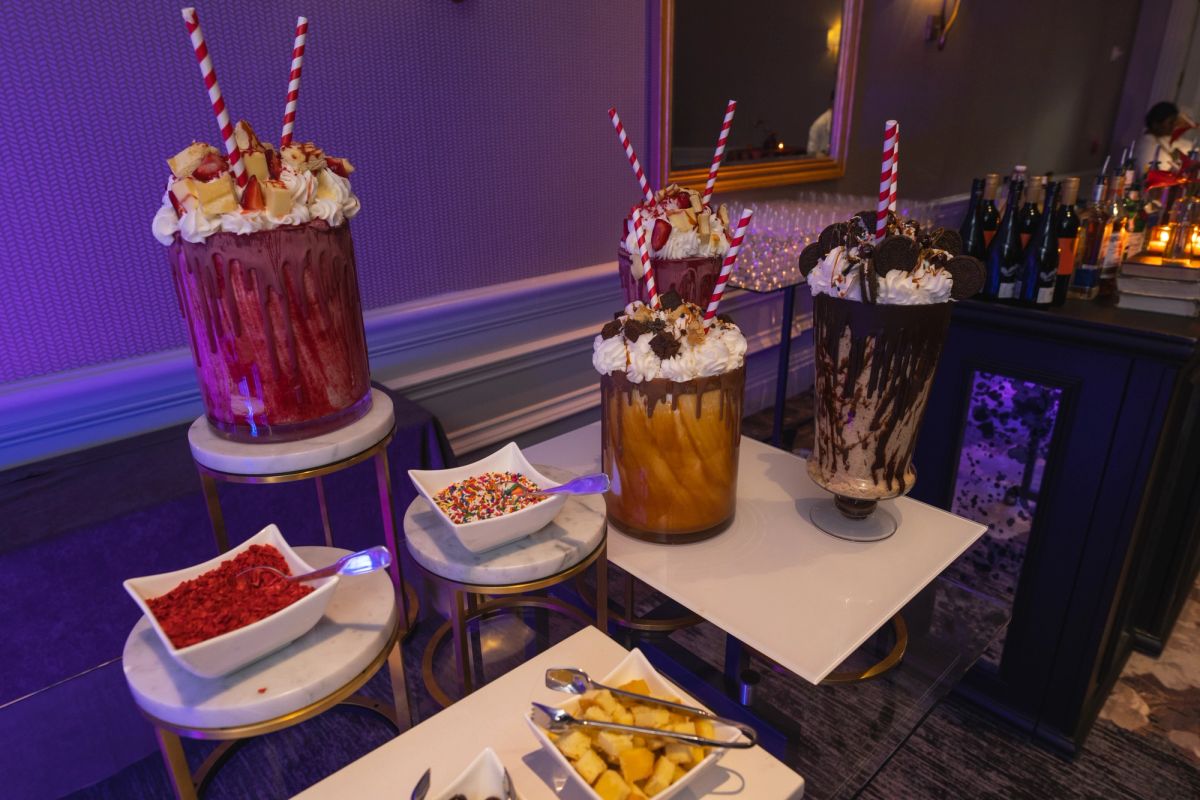 Elaborate milkshakes with whipped cream and striped straws displayed on small tables with colorful toppings.