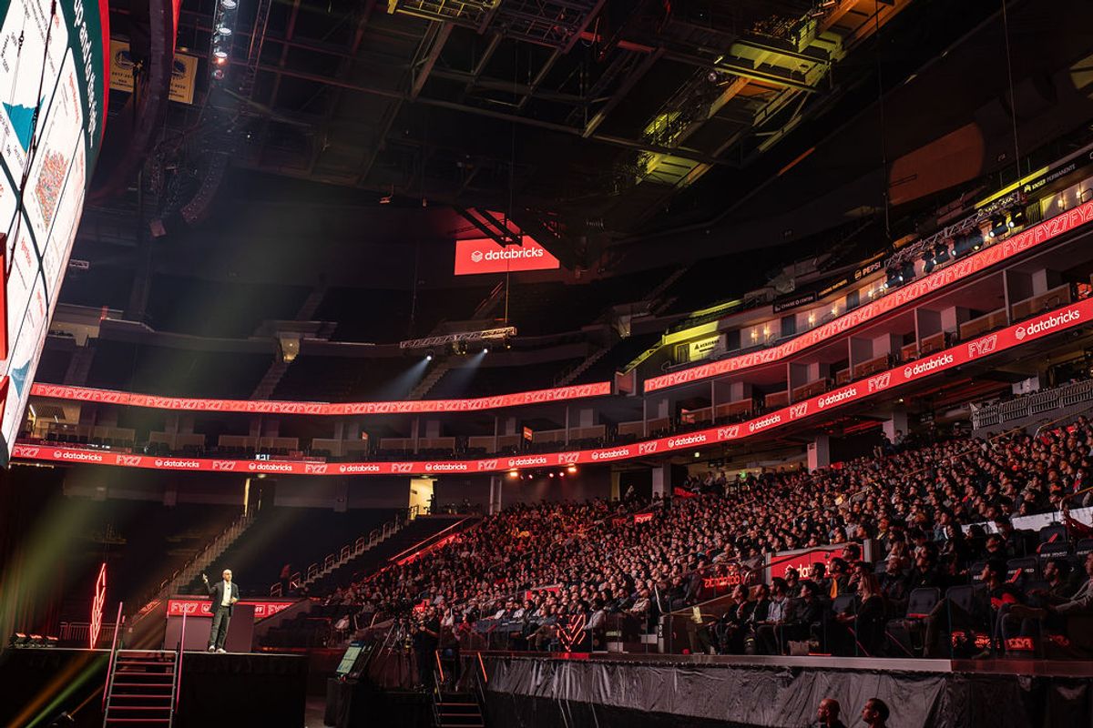 Speaker presenting to large audience in packed arena with red LED lighting and tiered seating