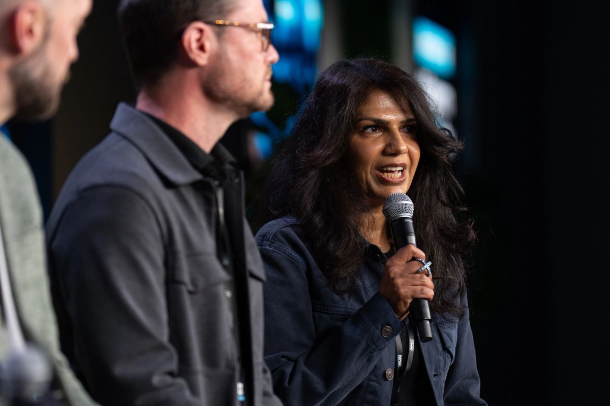 Woman speaking into microphone with man in glasses standing beside her at conference event