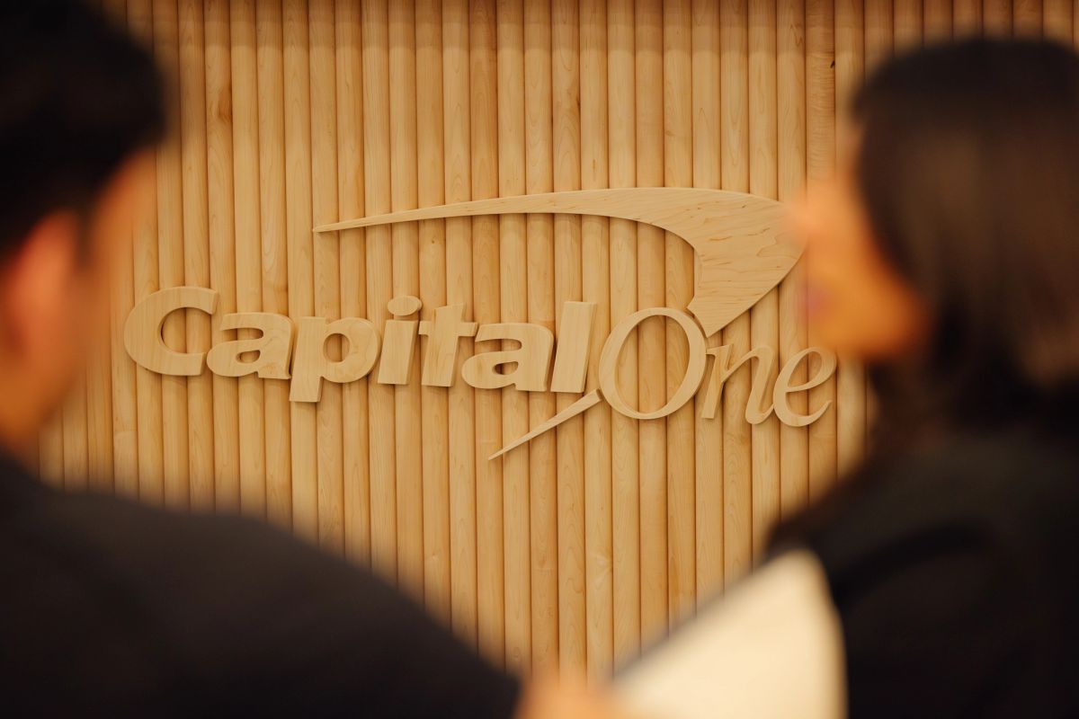 Two attendees view a wooden Capital One logo display at a conference event.