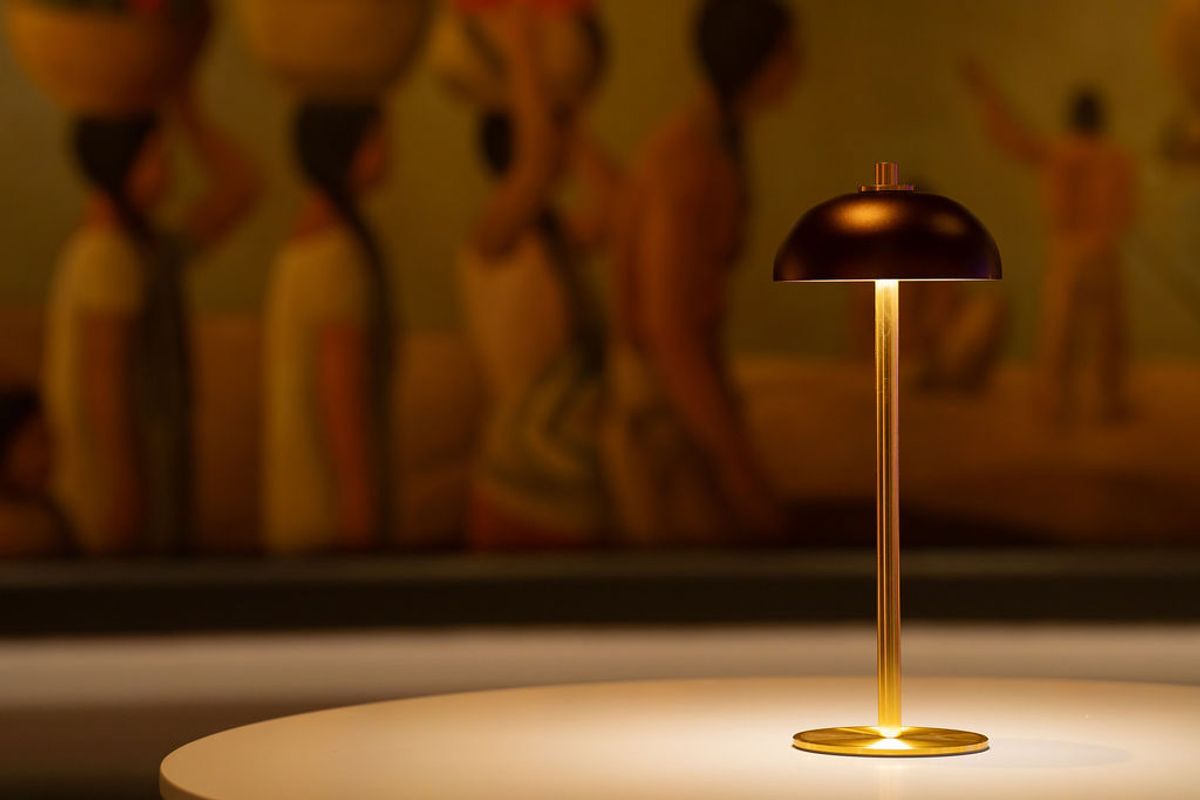 Modern brass table lamp with dome shade illuminated on white round table with blurred figures in background