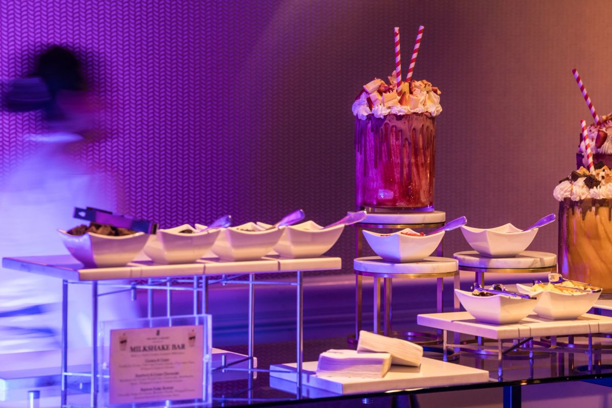 Dessert station with white bowls on tiered stands and milkshakes with striped straws under purple lighting