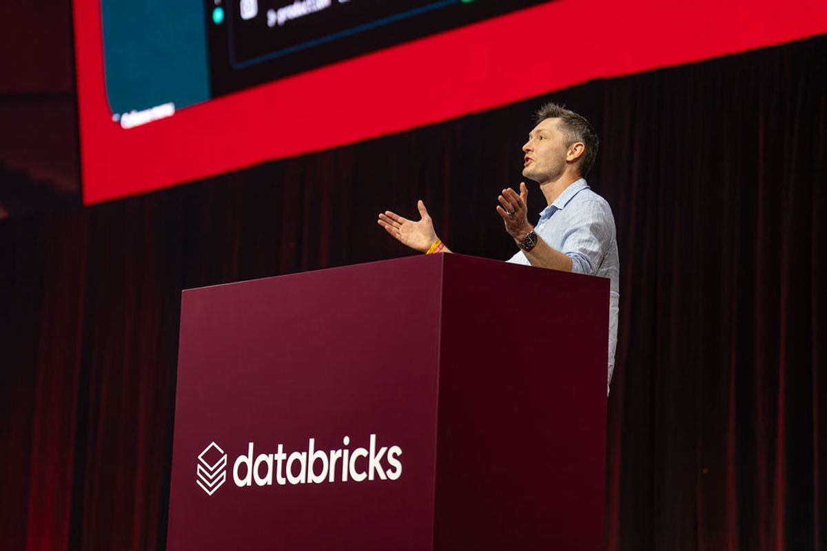 Speaker presenting at Databricks podium with large screen and red accent lighting in conference venue