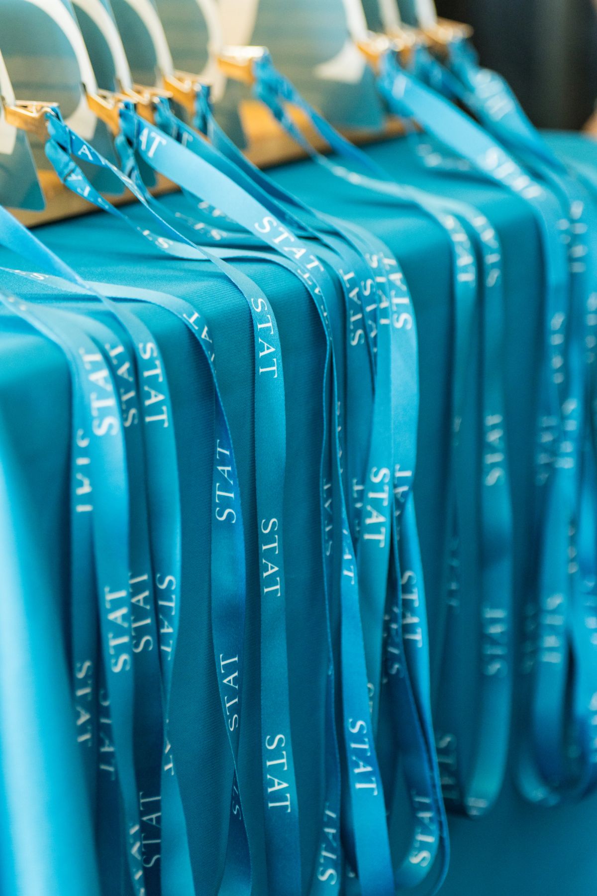 Blue conference t-shirts with "STAT" text hanging on white hangers at an event