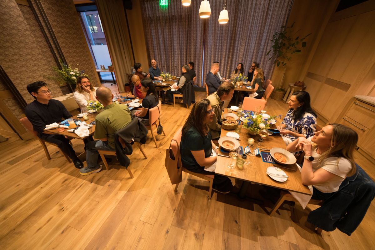 People seated around wooden tables in restaurant-style setting having dinner and discussion