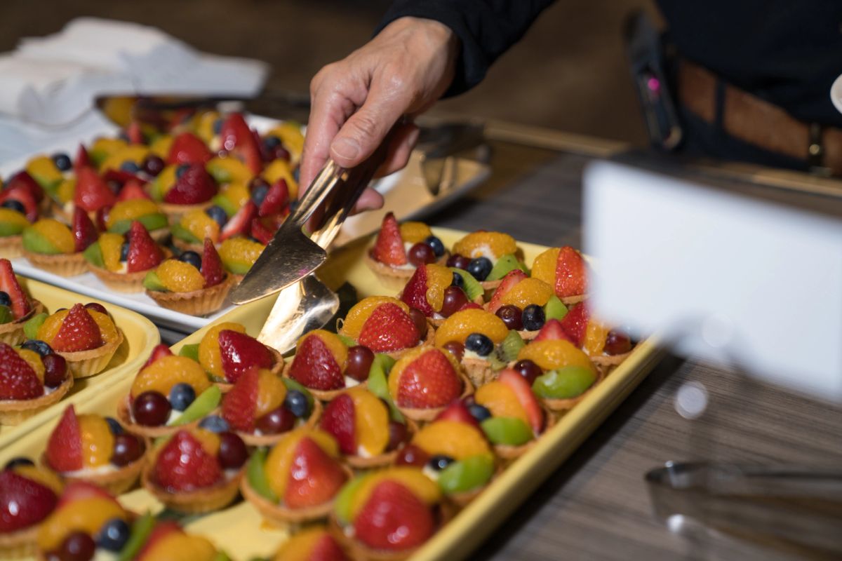 Catering staff serving colorful fruit tarts topped with strawberries, blueberries, and mandarin oranges.