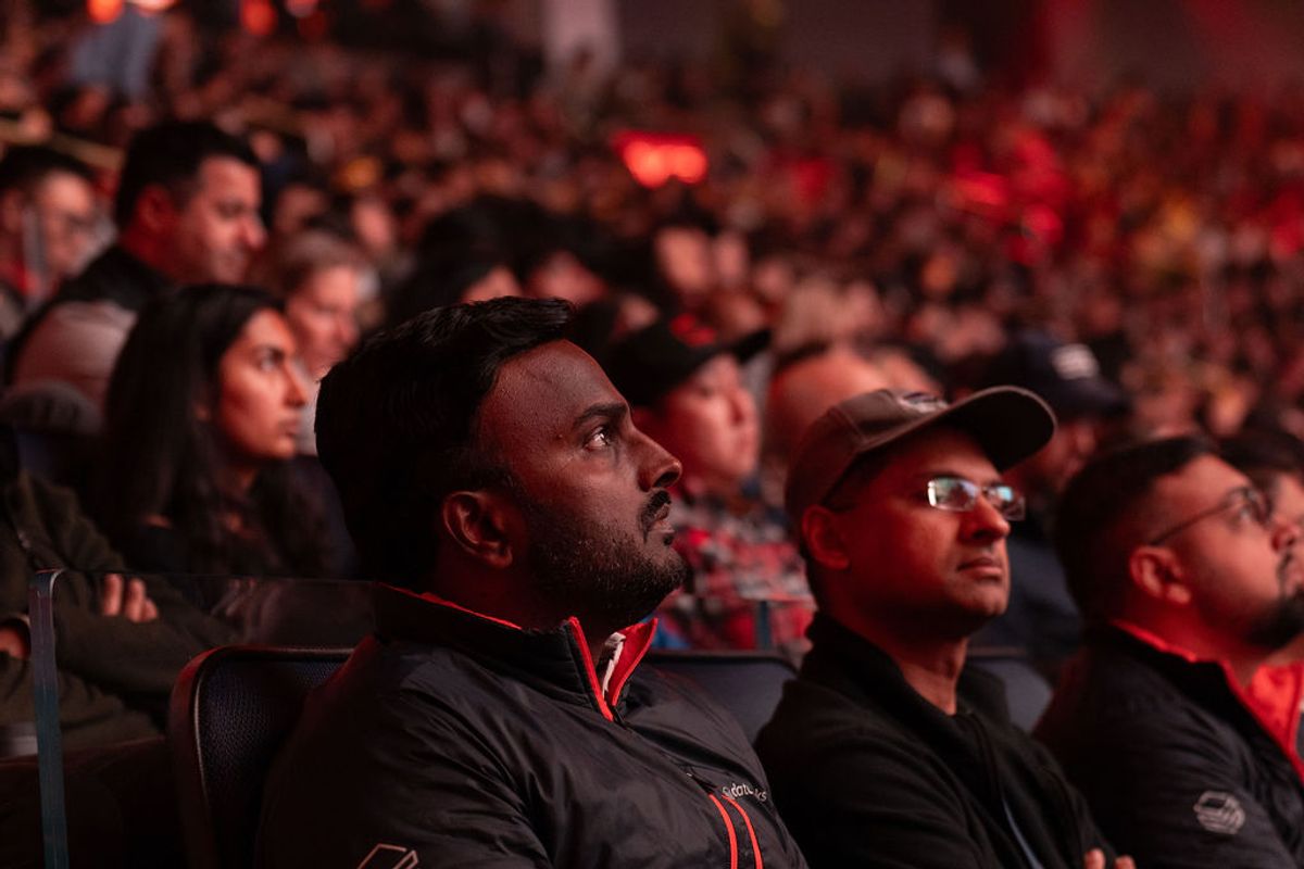 Audience members watching intently at a conference event, seated in dark venue with red stage lighting