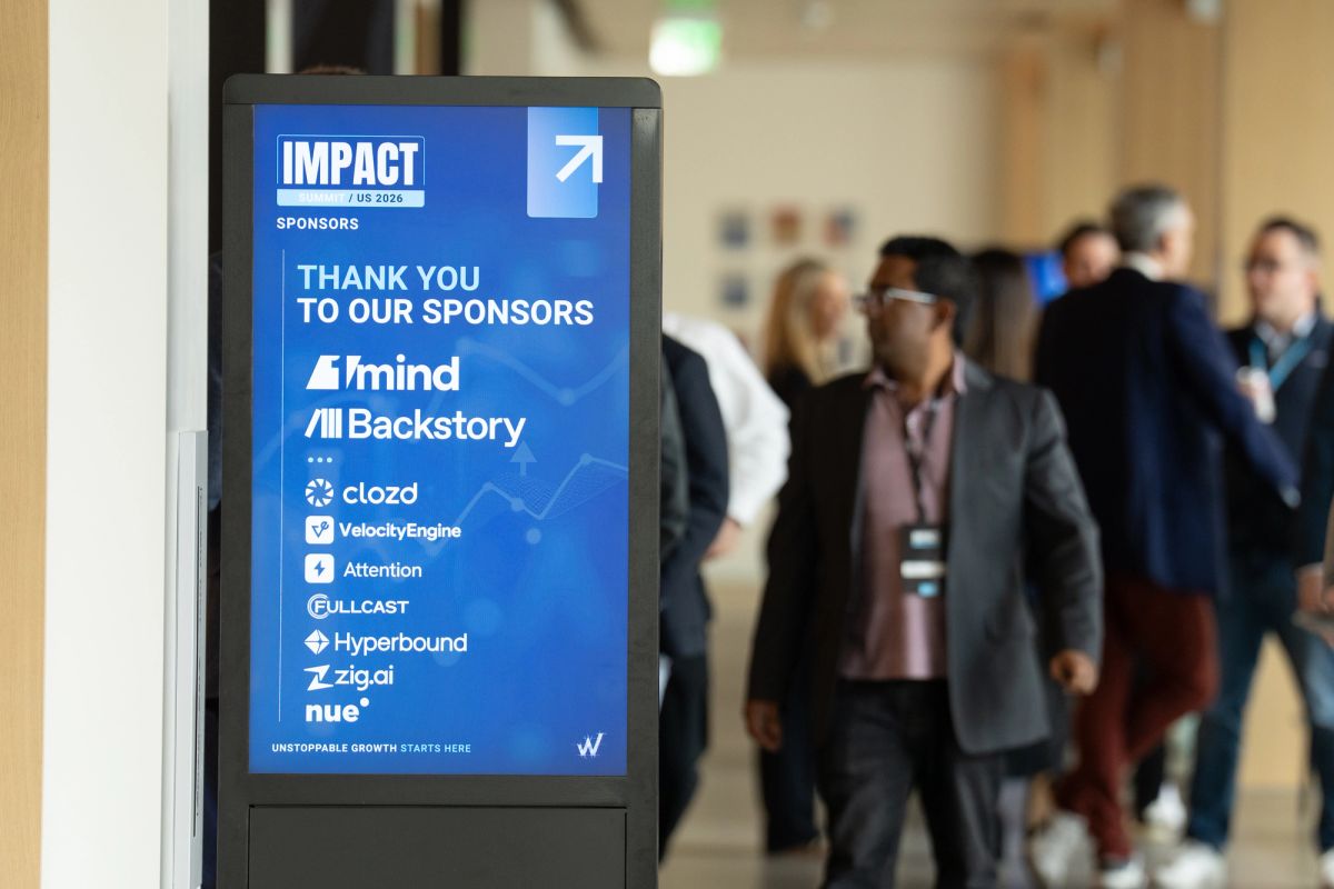 Digital display showing Impact conference sponsors with attendees walking in background at venue