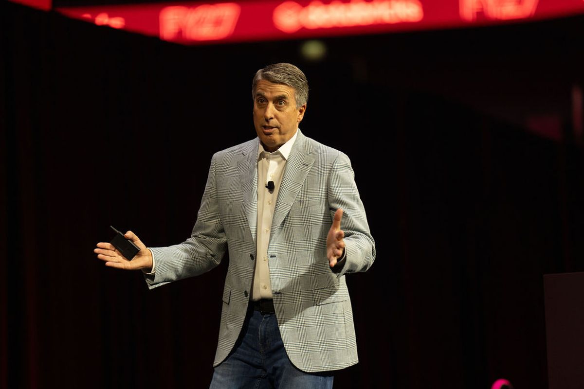 Speaker in gray suit jacket presenting on stage with red lighting in background