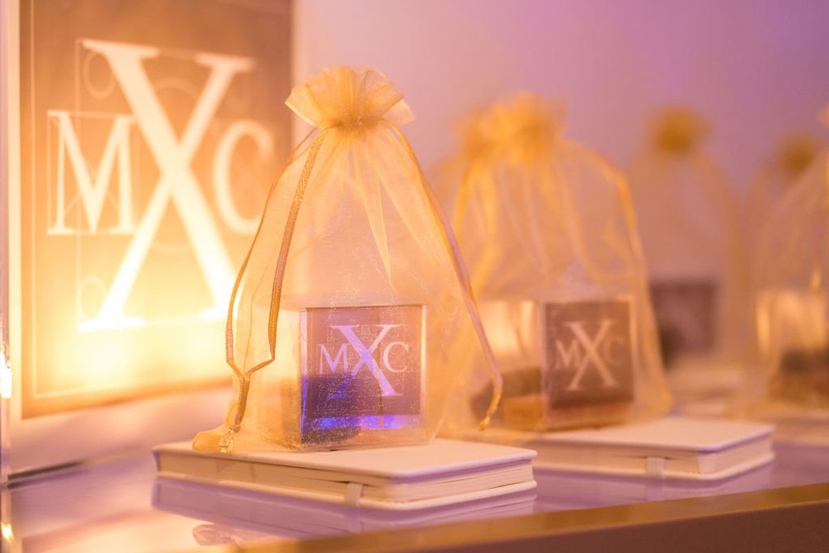 Small gift bags with MXC logos on wooden platforms at networking reception with warm lighting