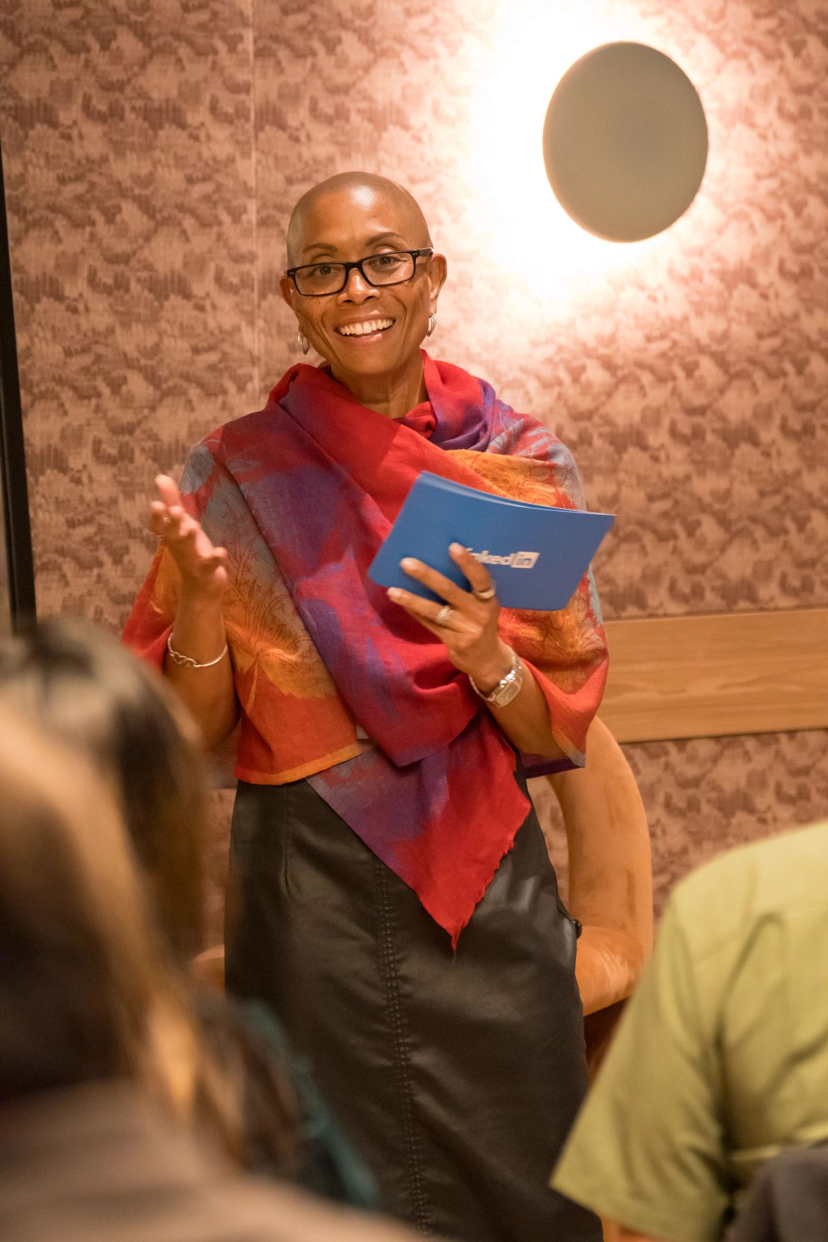 Speaker in colorful scarf gesturing with hand while holding blue book during panel discussion