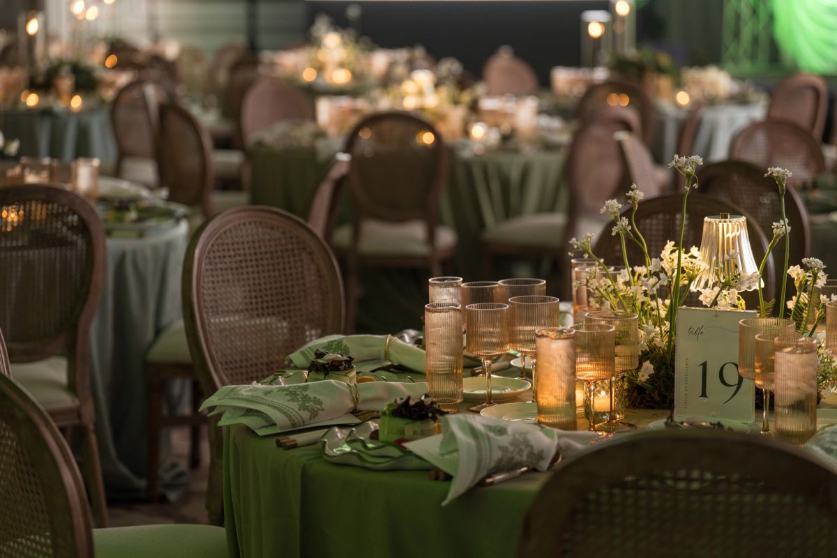 Elegant dinner tables with green linens, candles, and floral centerpieces set for an evening event