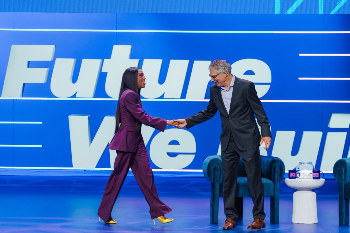 Two business professionals shake hands on stage in front of a blue backdrop with "Future" text visible
