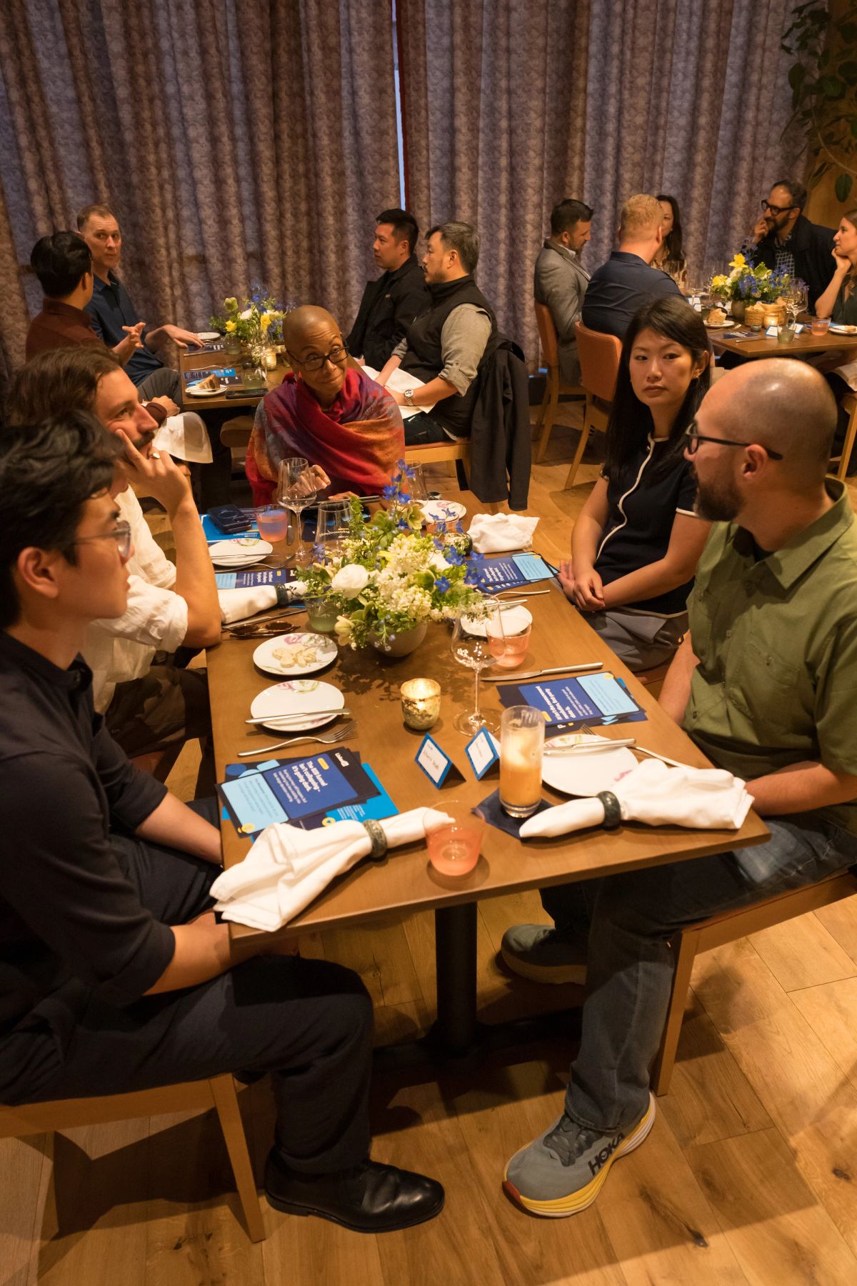 Panel discussion attendees seated around wooden tables with floral centerpieces and event materials