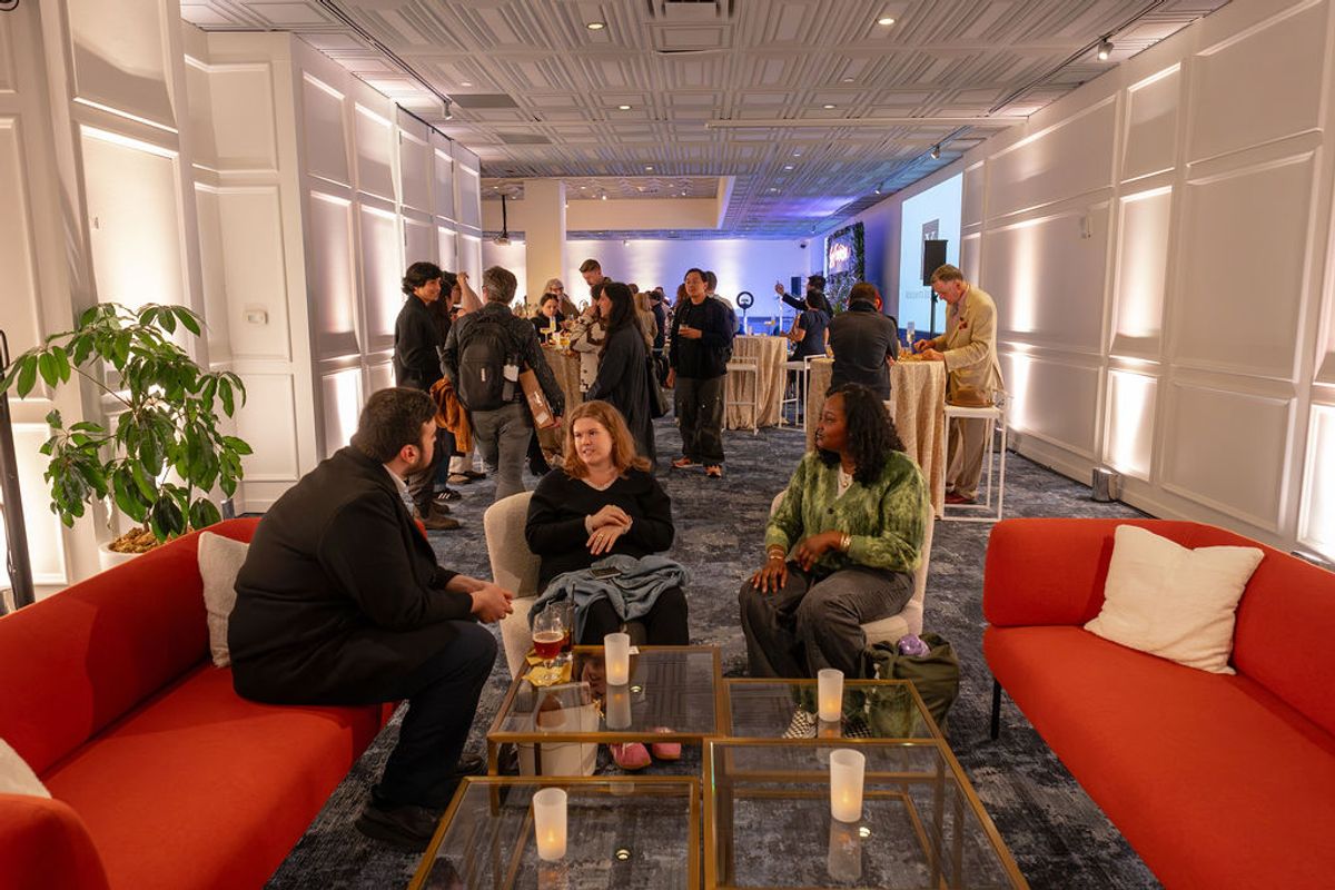 Attendees network at an upscale reception, with three people conversing on red sofas in foreground and groups.