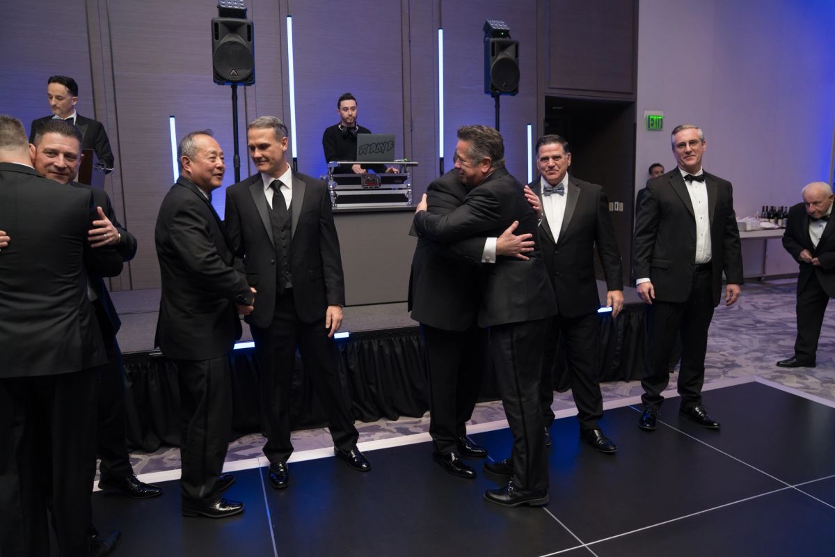 Men in black formal wear greeting each other with handshakes and embraces at an upscale event venue