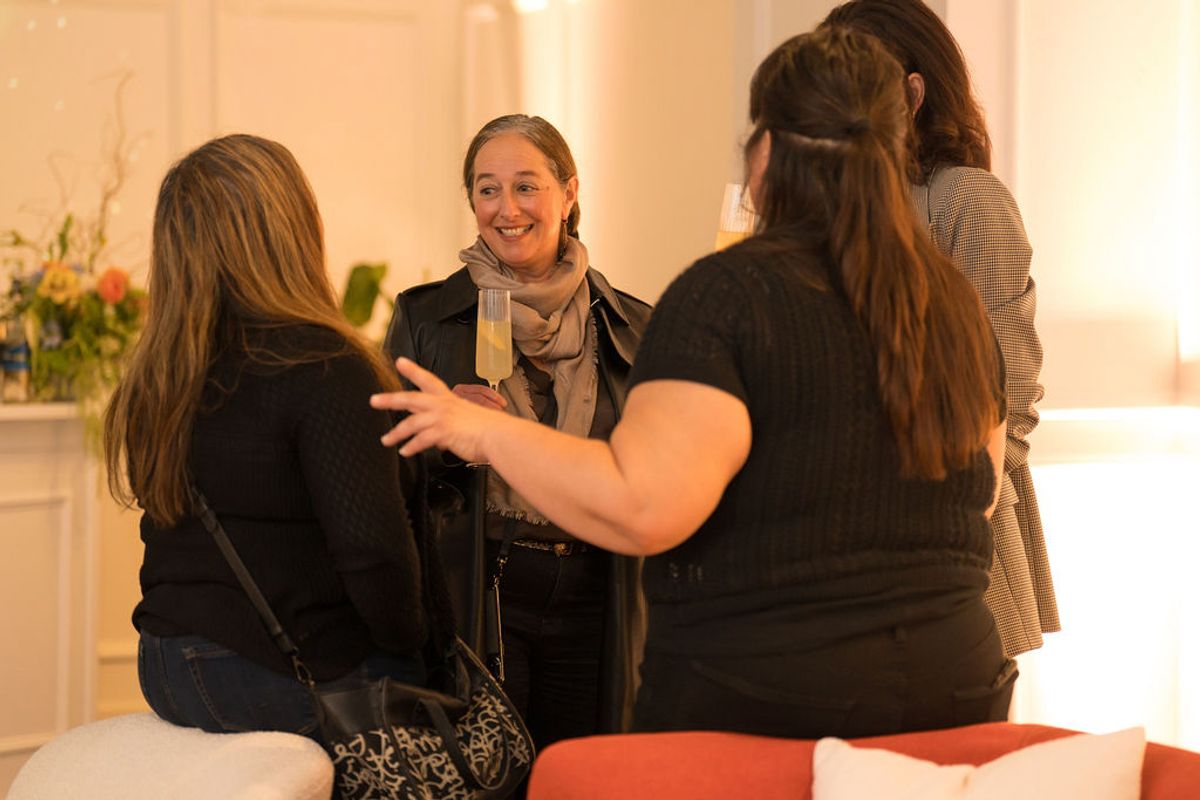 Four women networking and conversing at an indoor reception event with elegant lighting and floral decor.