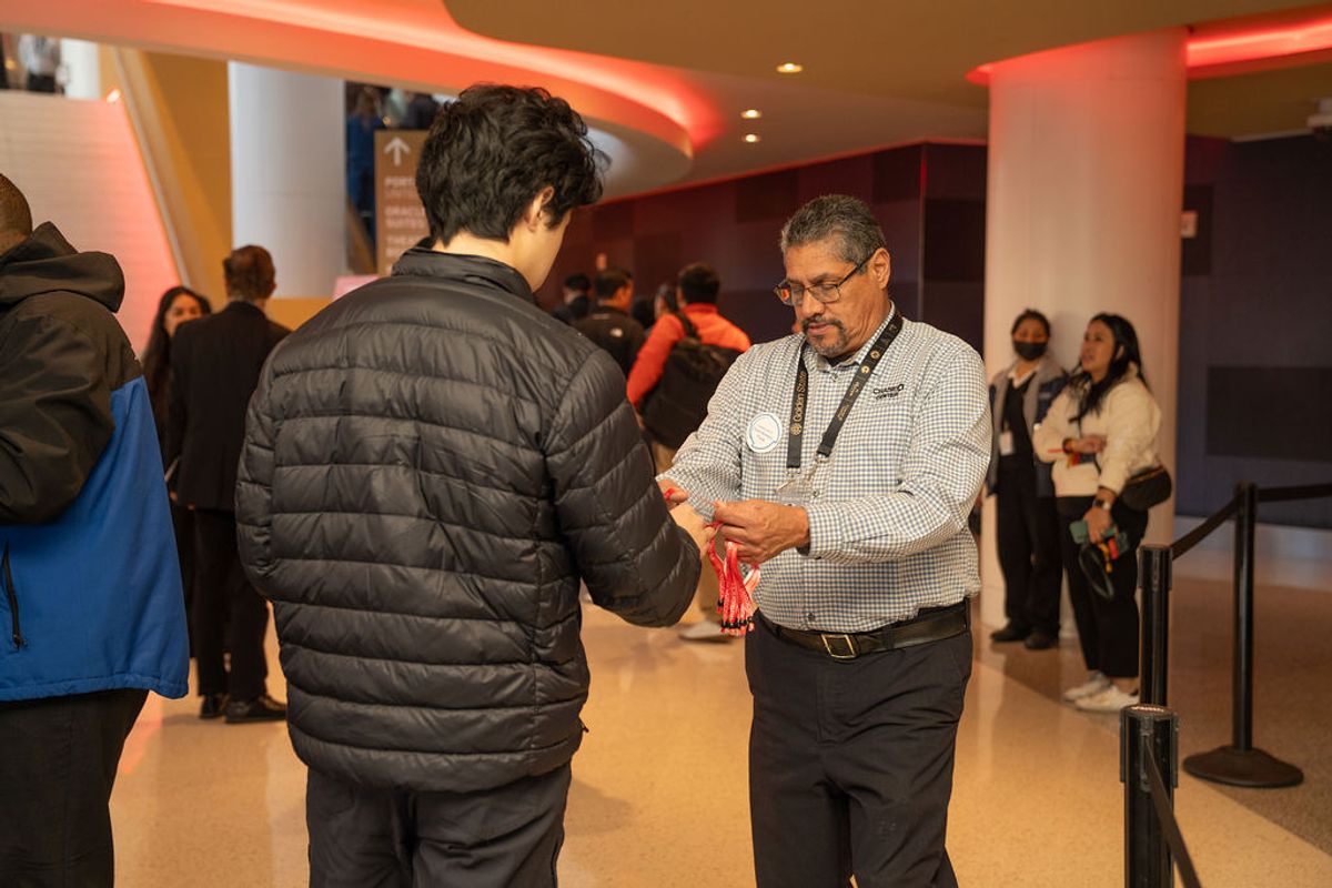 Staff member hands red lanyard to attendee in black jacket at conference venue with curved architecture