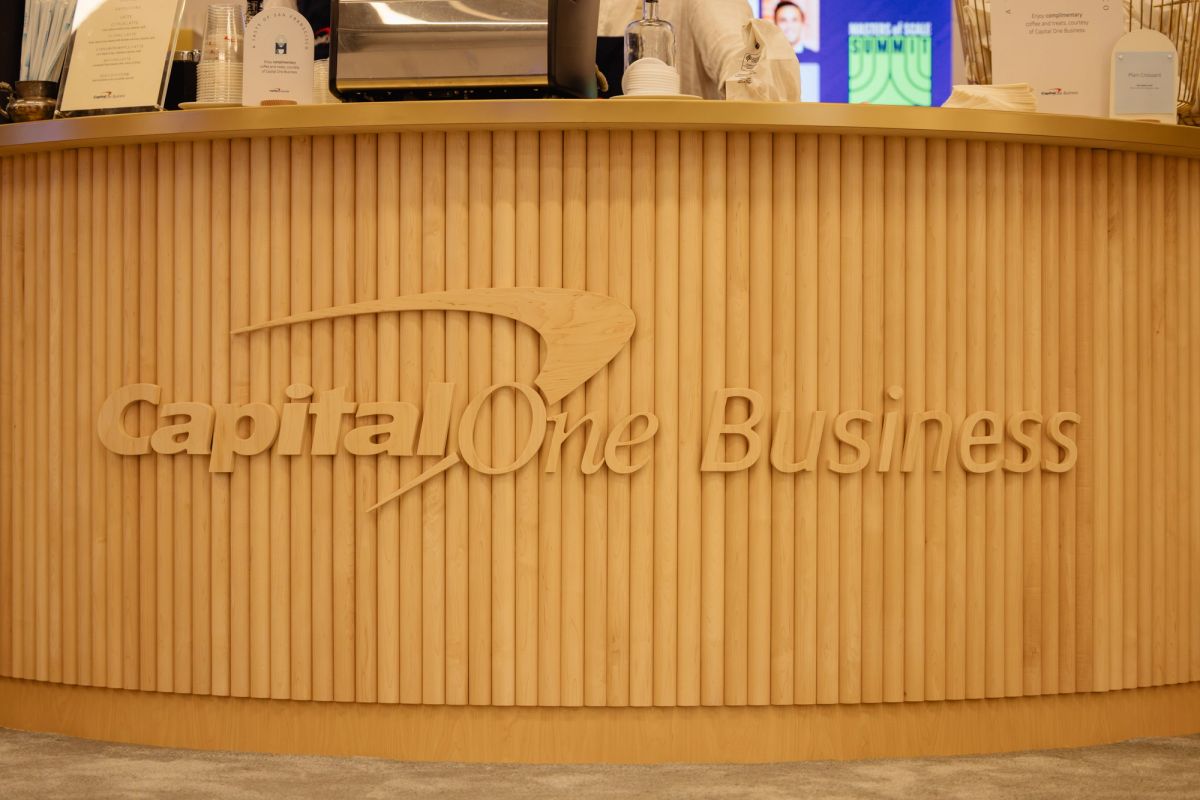 Curved wooden reception desk with "Capital One Business" carved text and vertical slat design