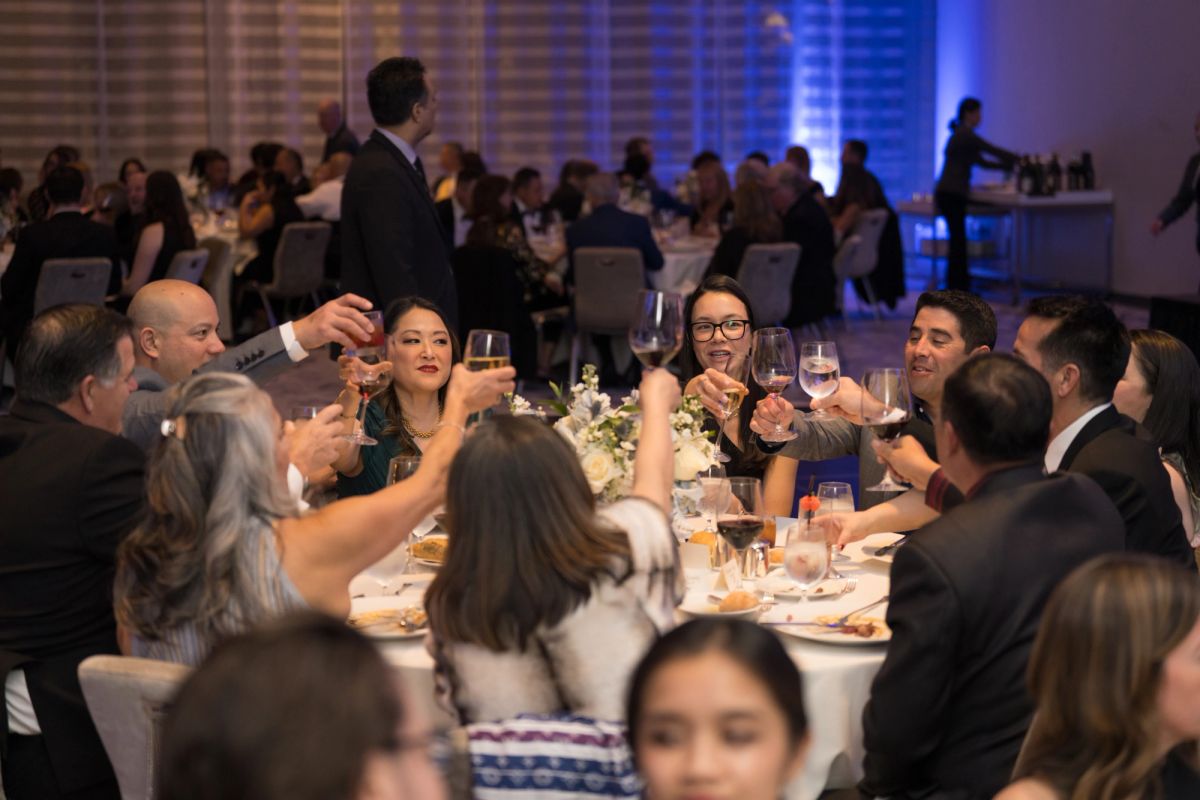 Guests raise champagne glasses in a toast at a formal dinner event with elegant lighting and decor.