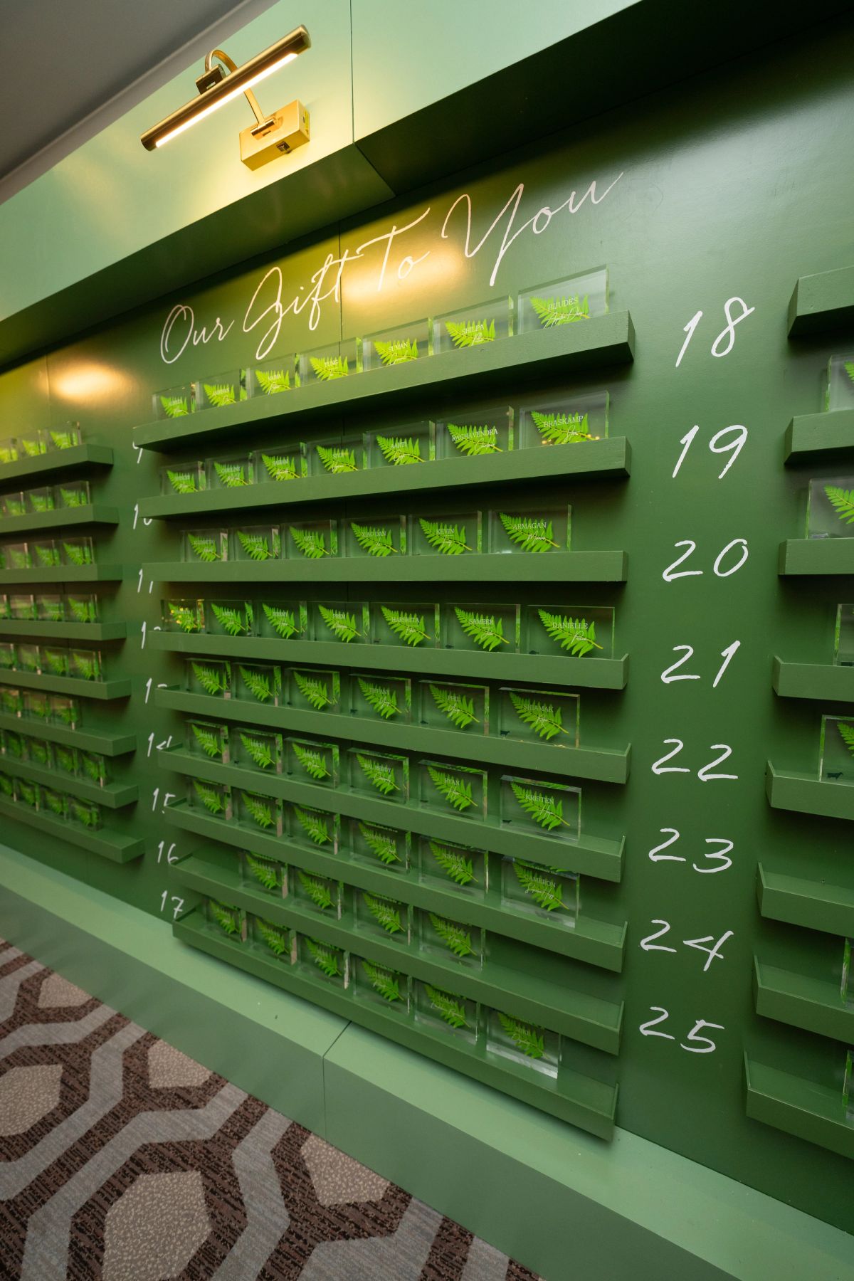 Green wall display with numbered shelves containing small fern plants, illuminated by warm lighting