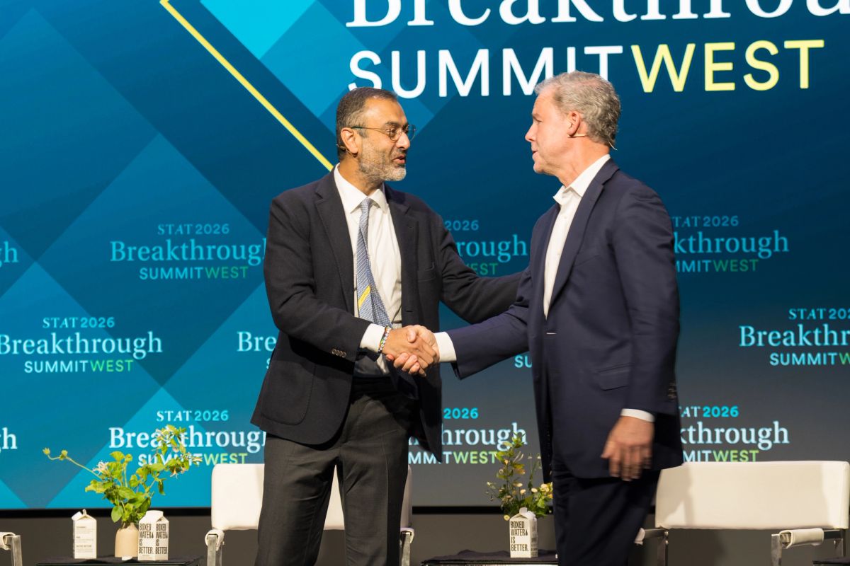 Two men in business suits shaking hands on stage at Breakthrough Summit West event with blue branded backdrop