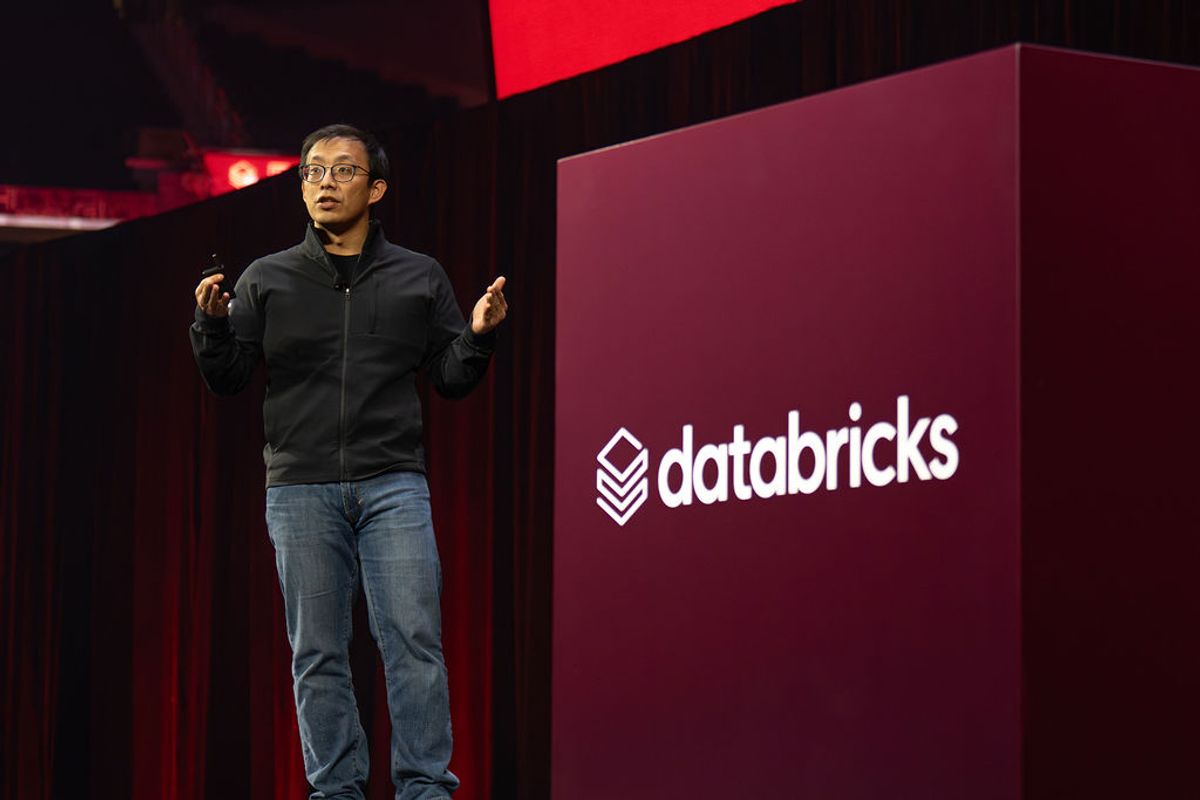 Speaker presenting on stage with Databricks logo backdrop at conference venue