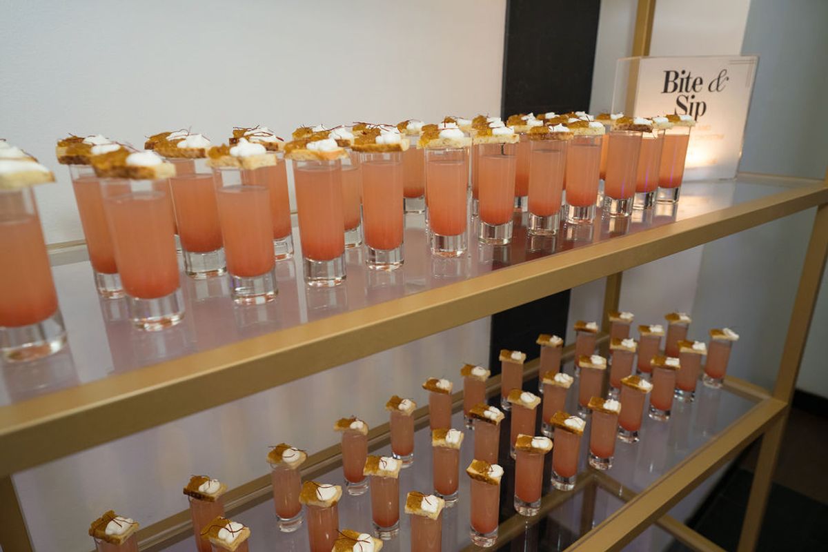 Two-tiered display of orange cocktails with white garnishes and "Bite & Sip" sign at networking event