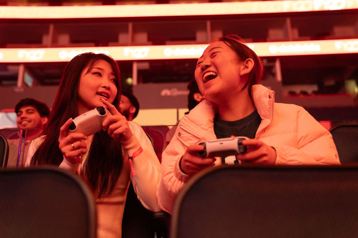 Two attendees laugh while holding gaming controllers at a conference event with red lighting