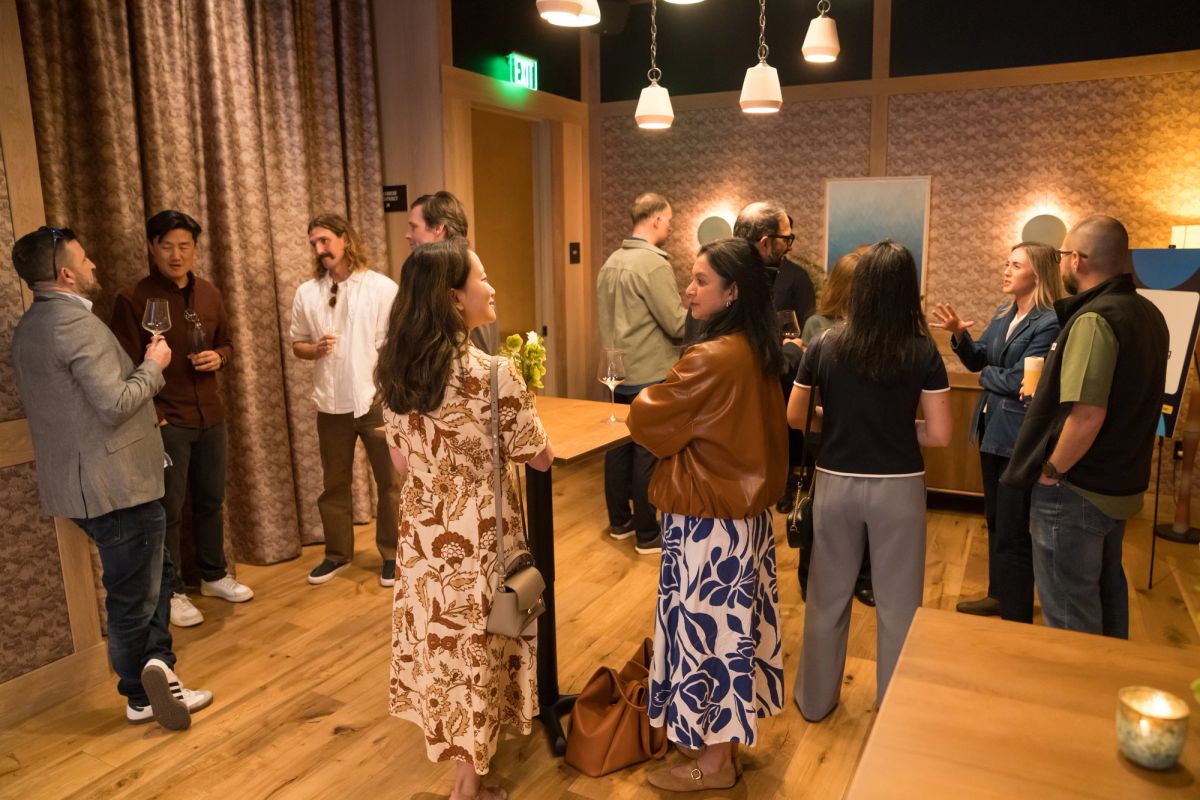 Attendees networking and conversing in groups at an indoor event with warm lighting and exposed brick walls.