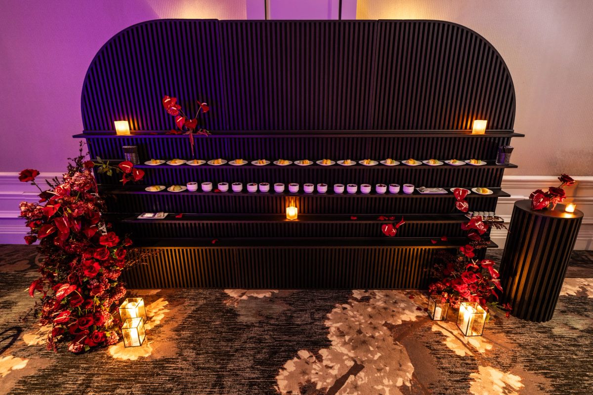 Dark display booth with tiered shelving, red floral arrangements, and warm lighting at indoor event