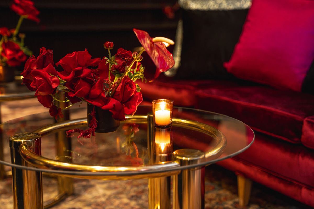 Glass coffee table with red flowers and lit candle, red velvet seating in background