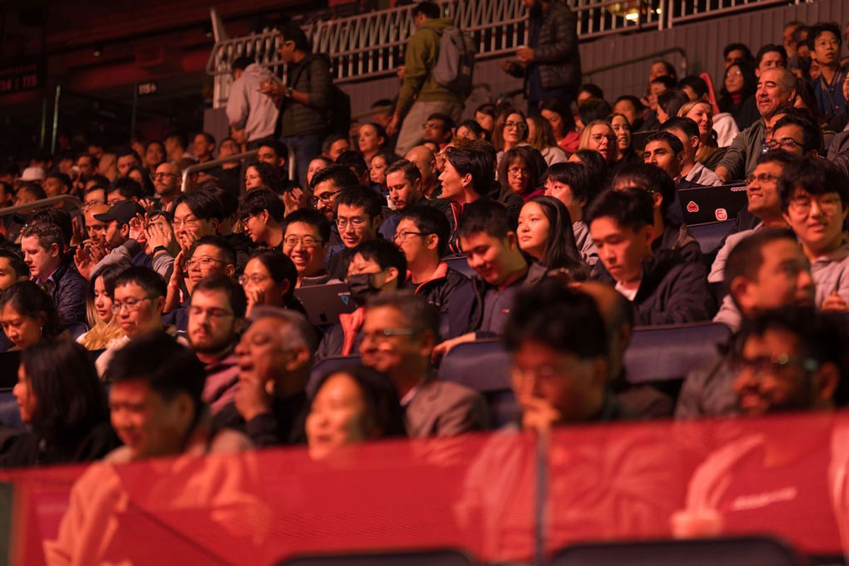 Audience members seated in tiered seating at a conference venue, with warm stage lighting illuminating the.