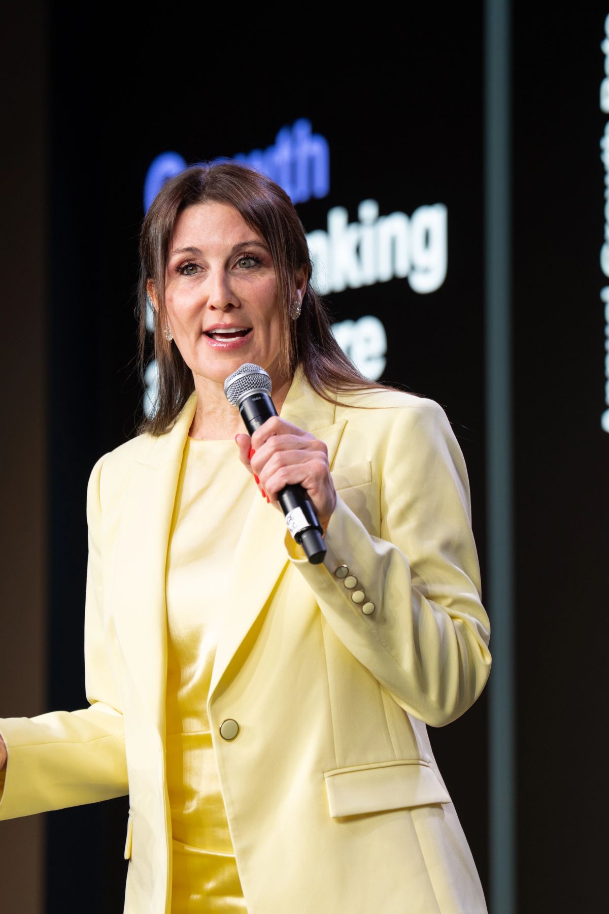 Speaker in yellow suit presenting with microphone at business conference