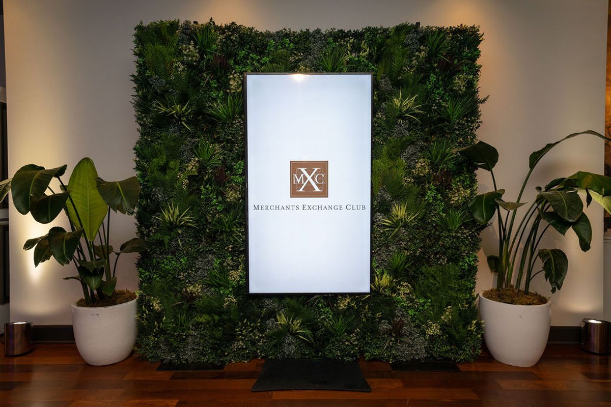 Green plant wall display with Merchants Exchange Club sign flanked by potted plants in modern interior