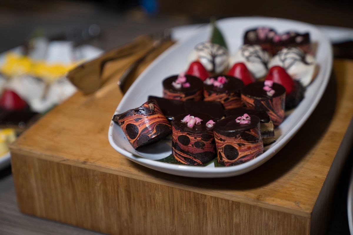 Elegant chocolate petit fours with pink flowers and red garnishes on a white platter atop a wood board.