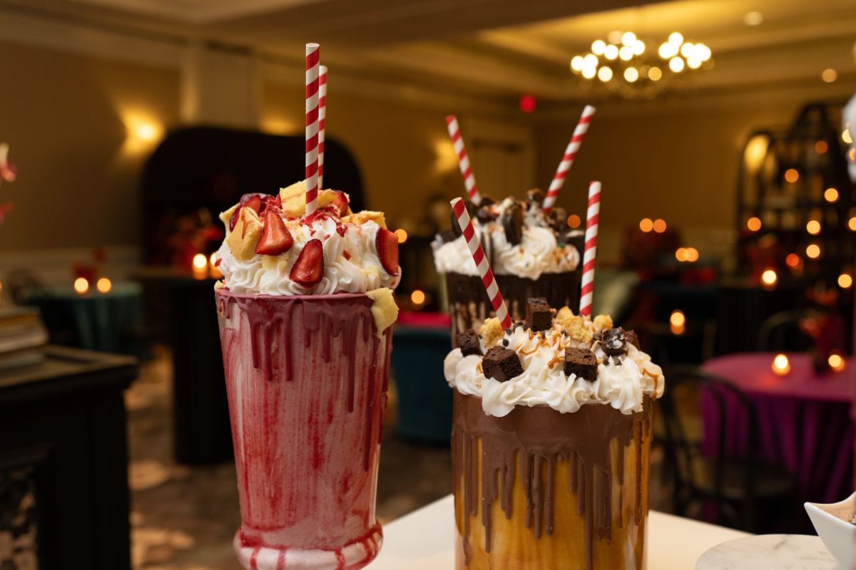 Two elaborate milkshakes with whipped cream, candy toppings, and striped straws on a table in an elegant.