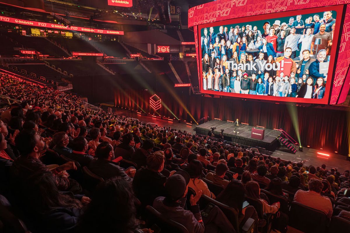 Large audience at conference event with speaker on stage and "Thank You!" displayed on overhead screen